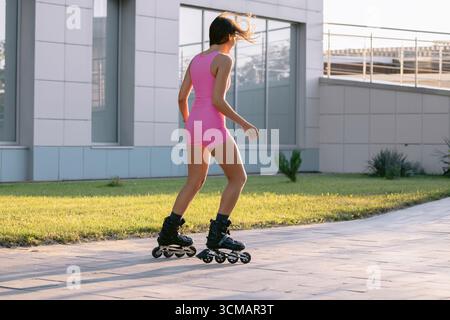 Young woman in pink sportswear rollerblading outdoors on a sunny day, active lifestyle and fitness concept. Stock Photo