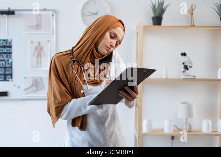 Muslim woman doctor with stethoscope making phone call talking with patient and taking notes. copy space Stock Photo