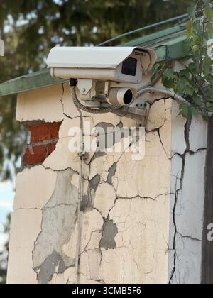 Security camera mounted on cracked building wall showing urban decay and infrastructure. Mobile photo Stock Photo