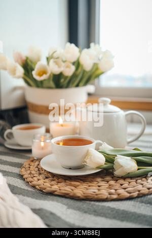 A cup of tea against the background of a basket with tulips in a cozy interior, spring still life. Stock Photo