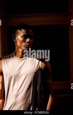 A striking portrait of a man wearing a sleeveless shirt, illuminated by warm, dramatic light. The contrast highlights his expressive face and toned ph Stock Photo
