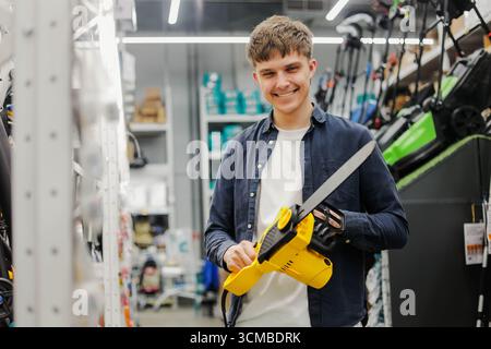 Young man choosing an electric chainsaw in a hardware store. Male customer standing in the power tools section, inspecting electric chainsaw Stock Photo