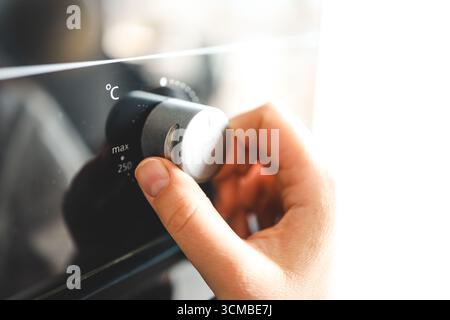 Women in modern kitchen turning on oven. Close up view of female hand and oven button. Stock Photo