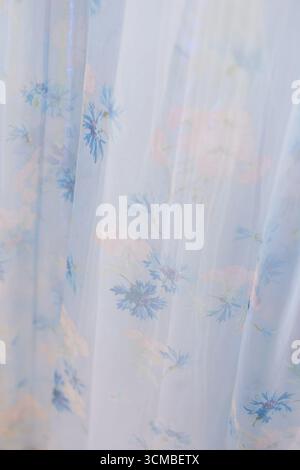 Delicate blue floral fabric hangs softly, catching light and adding a serene touch to the peaceful room environment. Stock Photo
