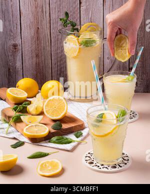 A refreshing lemonade pitcher with fresh lemons and mint, styled on a wooden table. Sliced lemons and mint leaves add a vibrant touch, evoking a summe Stock Photo