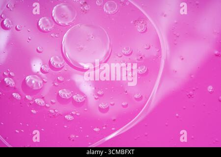 A vibrant pink liquid background featuring an array of water bubbles and light reflections, creating a dynamic and mesmerizing visual effect that embo Stock Photo