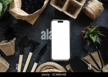 Phone with an isolated screen for your text on the background of garden tools. Stock Photo