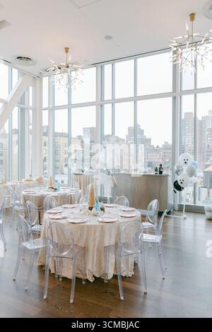 Bright dining area features round tables with lace decorations and city skyline views, ready for a festive gathering. Stock Photo