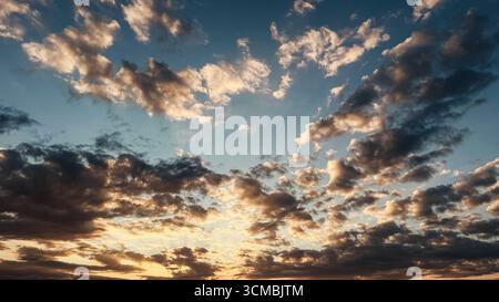 Dramatic sunset sky filled with scattered clouds illuminated by warm golden and blue hues in the evening light. Stock Photo