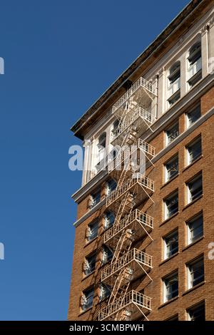 External fire escape on a brick-built building in Long Beach, California. The red brickwork of the building contrasts with the blue sky. Stock Photo