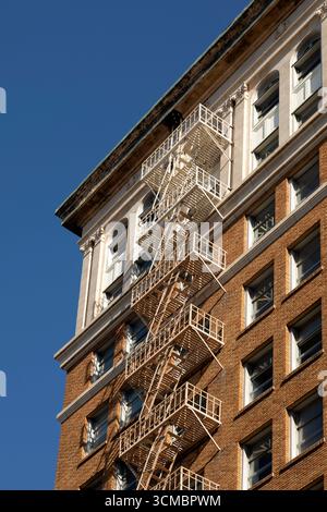 An external fire escape on a brick-built building in Long Beach, California. The red brickwork of the building contrasts with the blue of the sky. Stock Photo