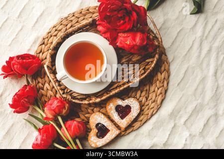 Tray with tasty breakfast, bouquet of peonies and gift for Valentine's Day on bed. Stock Photo