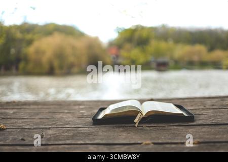 Open Bible on a wooden board near the river. Stock Photo