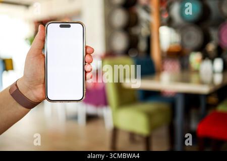 The girl holds a phone in her hands with a blank isolated screen on the background of food in a restaurant. Place for your menu or review. Stock Photo