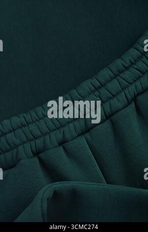 Warm dark green tracksuit. Close-up of elastic waistband. Textile warm fabric macro background. Cotton. Stock Photo