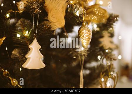 Ceramic ornament shaped like a Christmas tree hangs on a beautifully decorated evergreen, with golden accents and warm lights enhancing the festive am Stock Photo