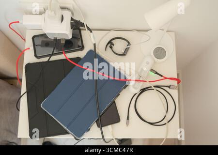 Overloaded power outlet. Multiple plugs, cords and electrical devices connected for charging to a multi-outlet wall outlet adapter in a bedroom at Stock Photo