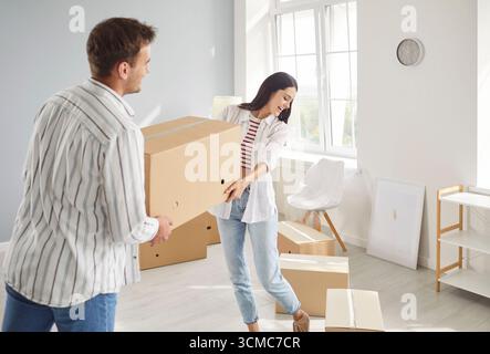 Young happy couple carrying cardboard box in new apartment on their moving day Stock Photo