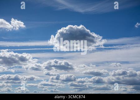 Single fluffy cloud floating in a bright blue sky. A natural background of summer weather and atmosphere. Stock Photo