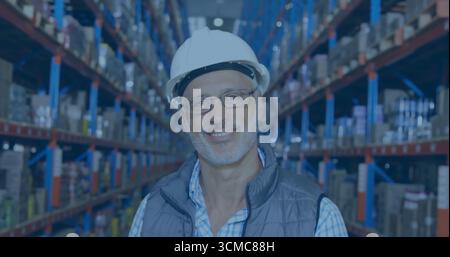 Standing man wearing white safety helmet and vest in warehouse, with shelves of boxes, containers Stock Photo