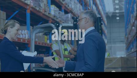 Shaking hands suited executives exchanging deal in warehouse aisle amid pallet racks and forklift Stock Photo