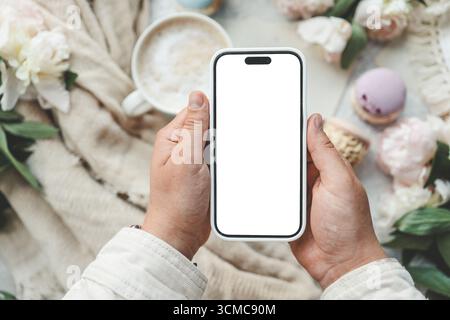 Phone in hands with an isolated screen on the background of a cup of coffee. Stock Photo