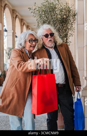 A joyful couple of seniors sharing a moment of excitement as they explore various shops, pointing at interesting items, and proudly carrying their Stock Photo