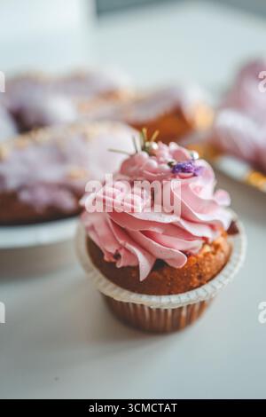 Vanilla cupcakes with cream cheese frosting and pink sprinkles on pink background. Saint Valentine's day or birthday dessert. Stock Photo