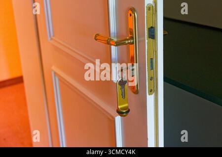 The same hotel door now stands open, the key and fob still in place. A warm corridor glows beyond the white frame. Brass hardware and clean lines make Stock Photo