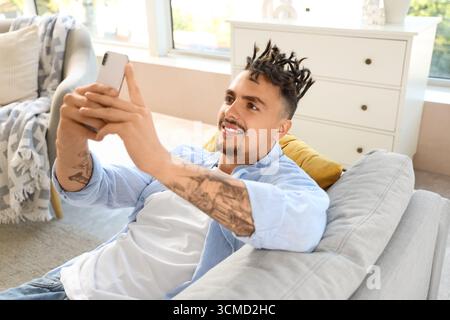 Young man with dreadlocks using mobile phone on sofa at home Stock Photo