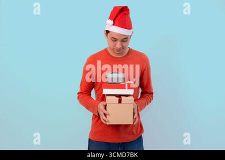 happy young man in santa hat holding holiday gifts against blue background Stock Photo