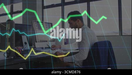 Man wearing dress shirt writing in notebook using dual monitors at office desk, copy space Stock Photo