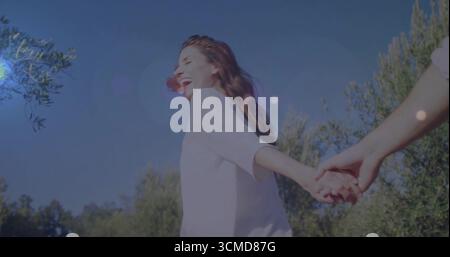 Smiling mid adult Hispanic woman leading man through sunlit garden grove, with connected hands Stock Photo