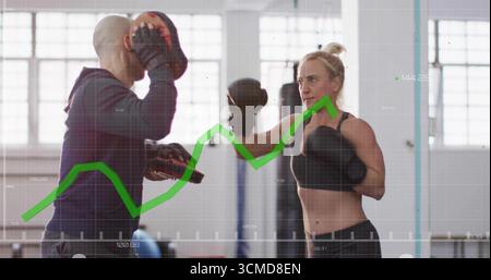 Holding focus mitts, trainer guiding gloved boxer delivering punch in gym, with green graph overlay Stock Photo