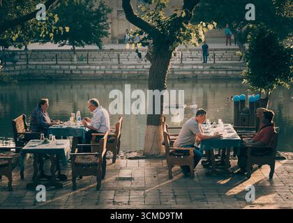 Group of Uzbek adults including elderly and middle-aged people dine at tables by Lyab-i-Hauz pool in Bukhara, Uzbekistan, with food, drinks. Stock Photo