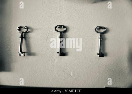 Black and white photograph of three vintage keys on a wall Stock Photo