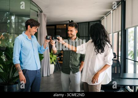 Happy creative diverse colleagues having fun while talking and drinking coffee, tea in working break Stock Photo