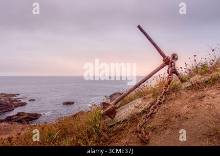 Old Rusty Ship Anchor With Heavy Chain On Rocky Coastline At Sunset. Maritime Heritage, Weathered Metal, Atlantic Shore, Nautical History, Abandoned Stock Photo