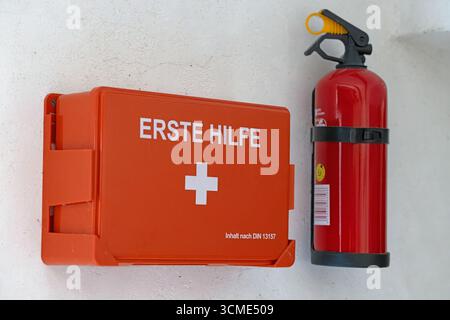 Mounted first aid box and red fire extinguisher on wall for workplace emergency safety Stock Photo