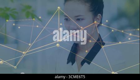 Office worker wearing blazer analyzing data on monitor and keyboard at office desk, network overlay Stock Photo
