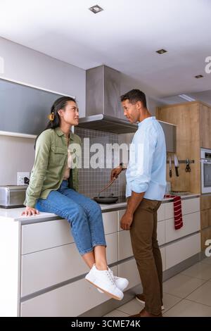 Asian couple chatting and cooking breakfast in modern home kitchen with frying pan Stock Photo