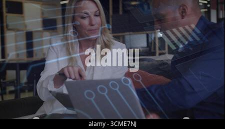Reviewing data on laptop and tablet on office bench in blazers, colleagues using digital overlays Stock Photo