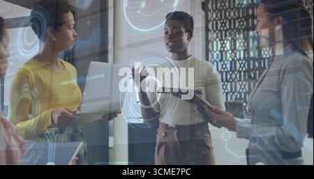 Collaborating three women presenting data on holographic display in office, with laptop and tablet Stock Photo