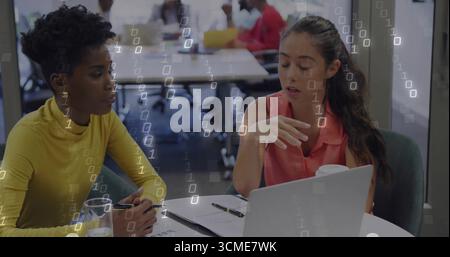 Discussing project details women sitting at table in open-plan office with laptop and documents Stock Photo