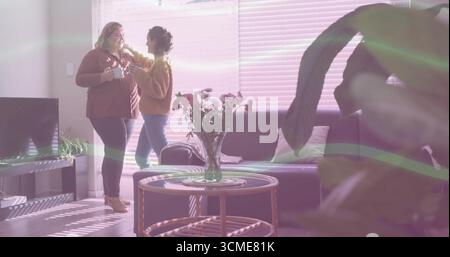 Chatting friends holding white mugs and adjusting hair in living room with coffee table, copy space Stock Photo