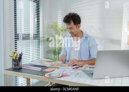 A focused designer is working on UX/UI design ideas, analyzing color palettes and interface structures pinned on a board. The scene reflects creativit Stock Photo