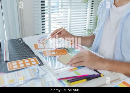 A focused designer is working on UX/UI design ideas, analyzing color palettes and interface structures pinned on a board. The scene reflects creativit Stock Photo