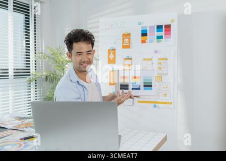 A focused designer is working on UX/UI design ideas, analyzing color palettes and interface structures pinned on a board. The scene reflects creativit Stock Photo