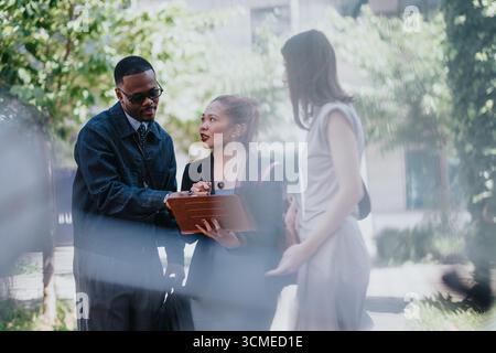 Diverse colleagues collaborating outdoors on a project featuring a digital tablet Stock Photo