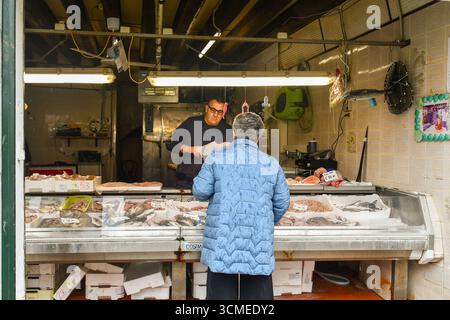 An elderly lady from behind buying fresh fish from a fishmonger at Fondamenta Sant'Anna, in the sestiere of Castello, Venice, Veneto, Italy Stock Photo